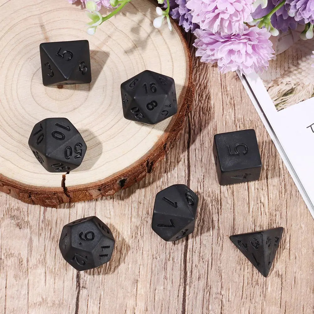 Black polyhedral dice set with seven pieces for D&D and tabletop RPGs, featuring numbers and symbols on each die.